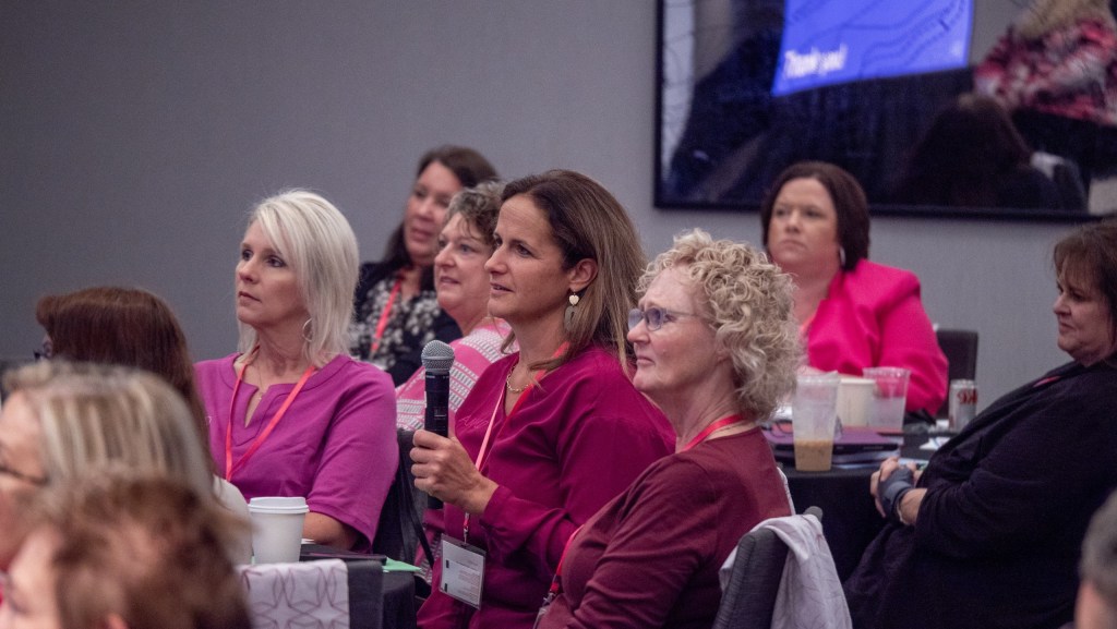 Multiple women wearing pink listen intently.